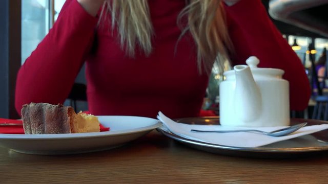 A woman sits at a table with meal in a cafe, drinks tea, refills the cup and drinks again - closeup