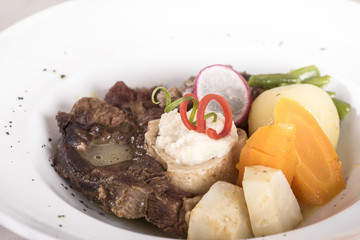 Baked beef marrow with vegetables, decorated with purple leafs, placed on white plate, light background, isolated