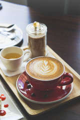 red coffee cup latte art and cake on wood table in coffee shop vintage style