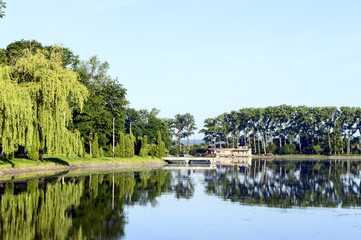 Lake, old pier, green trees, blue sky