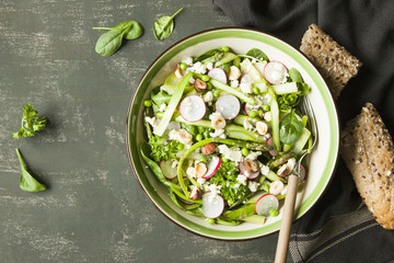 Spring vegetable salad with asparagus, zucchini, radish, spinach and goat cheese on dark background.