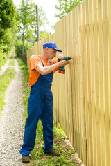 Full-length portrait of worker constructing wooden fence with a screwdriver