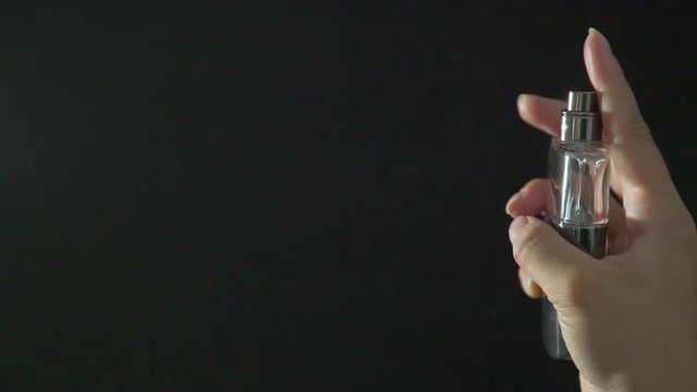 Splash of eau de toilette against a black background isolated. Female hands hold a bottle of perfume, spray it to feel fragrance. Aroma of eau de toilette: splashes on a black background.
