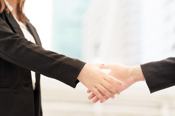 Close up of two smile businesswoman shaking hands on blurred building background.