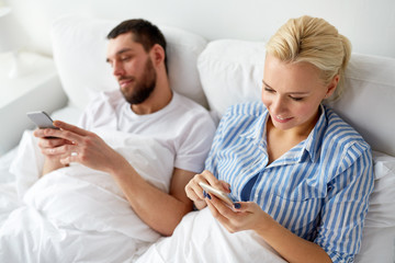 Obraz premium couple with smartphones in bed at home
