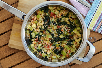 Delicious homemade vegetarian bulgur (couscous) with vegetables:spinach, carrots, zucchini, tomatoes and dill in pan - top view.