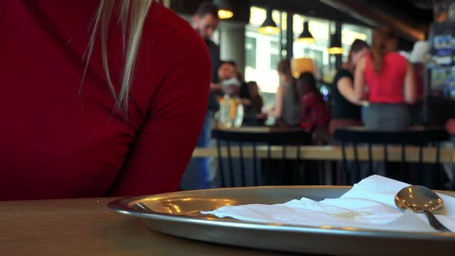 A woman sits at a table in a cafe and drinks tea, other customers in the blurry background - closeup on the cup