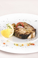 Grilled carp, served with lemon and decorated with radish and fresh leafs, light background, isolated