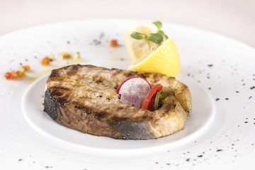 Grilled carp, served with lemon and decorated with radish and fresh leafs, light background, isolated