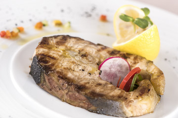 Grilled carp, served with lemon and decorated with radish and fresh leafs, light background, isolated