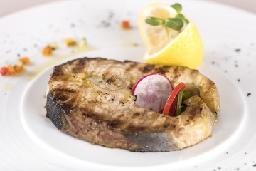 Grilled carp, served with lemon and decorated with radish and fresh leafs, light background, isolated