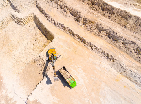 Aerial view of a excavator loading a truck in open cast mine or on construction site. Heavy industry from above. Industrial background from drone. 