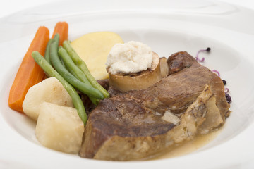 Baked beef marrow with vegetables, decorated with purple leafs, placed on white plate, light background, isolated