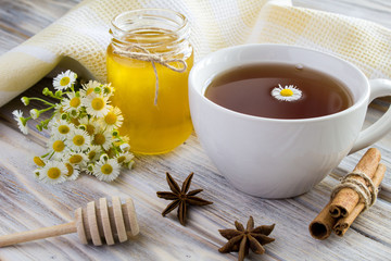 Tea, honey, cinnamon and chamomiles on the wooden background 