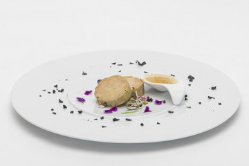 Liver terrine served with sweet sauce, decorated with flower petals, green leafs and black salt, placed on white plate, light background, isolated