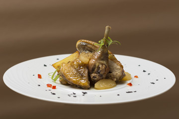 Roasted guinea fowl with potatoes, with green herbs, placed on a white plate, brown background
