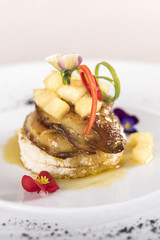 Luxurious dish with duck liver, pineapple and mango pieces, sweet sauce, placed on toasted bread, decorated with eatable flowers and red and green leafs, placed on white plate, light background, isola