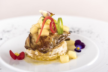 Luxurious dish with duck liver, pineapple and mango pieces, sweet sauce, placed on toasted bread, decorated with eatable flowers and red and green leafs, placed on white plate, light background, isola