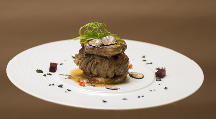 Sliced truffles topped on a grilled steak, beef and pork, with vegetable and sauce, on a white plate, brown background