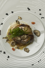 Sliced truffles topped on a grilled steak, beef and pork, with vegetable and sauce, on a white plate, brown background