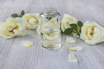 vial with tea roses essential oil on light wooden background
