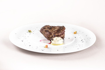 Succulent beef tenderloin steak, served with butter with herbs, decorated with radish and red and green herbs, placed on a white plate, light background, isolated