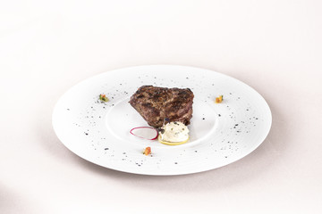 Succulent beef tenderloin steak, served with butter with herbs, decorated with radish and red and green herbs, placed on a white plate, light background, isolated