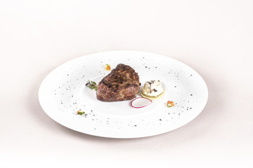 Succulent beef tenderloin steak, served with butter with herbs, decorated with radish and red and green herbs, placed on a white plate, light background, isolated