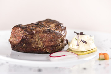 Succulent beef tenderloin steak, served with butter with herbs, decorated with radish and red and green herbs, placed on a white plate, light background, isolated