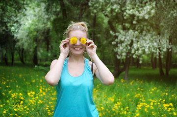 cheerful girl in the blue shirt keeps dandelions from the eye. Funny woman in an Apple orchard on the green lawn