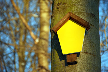 Small signboard with a wooden roof and yellow surface for self-marking, mounted on a tree in the forest 