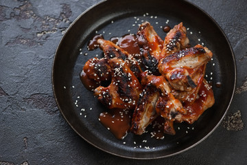 Metal plate with grilled chicken wings with sauce and sesame on a brown stone background, horizontal shot
