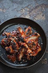 Barbecued chicken wings served with sauce and sesame seeds on a metal plate, vertical shot