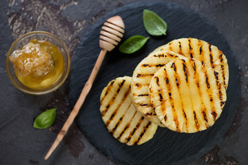 Top view of grilled sliced pineapple served with honey and basil on a stone slate tray