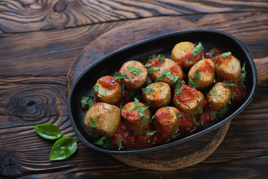 Cast-iron frying pan with sicilian style cooked potato, rustic wooden setting, studio shot