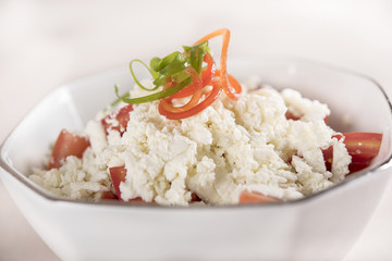 Simple tomato and cheese salad, decorated with green and red leafs, placed on a white plate, light background