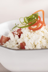 Simple tomato and cheese salad, decorated with green and red leafs, placed on a white plate, light background