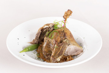 Traditional dish with baked drumstick duck and sour cabbage, decorated with herbs, placed on white plate, light background, isolated