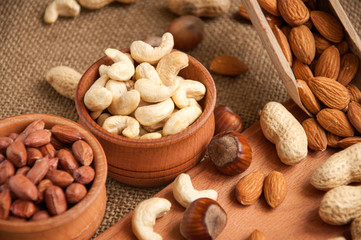 Almonds, cashew and hazelnuts in wooden bowls on wooden and burlap, sack background
