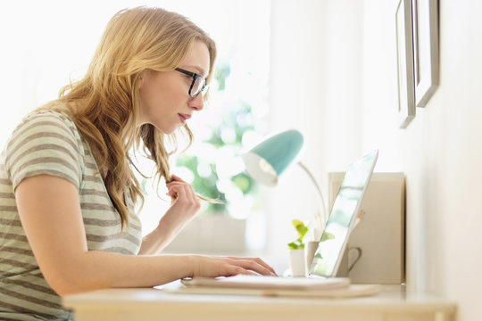 Side-view of young woman working on laptop at home