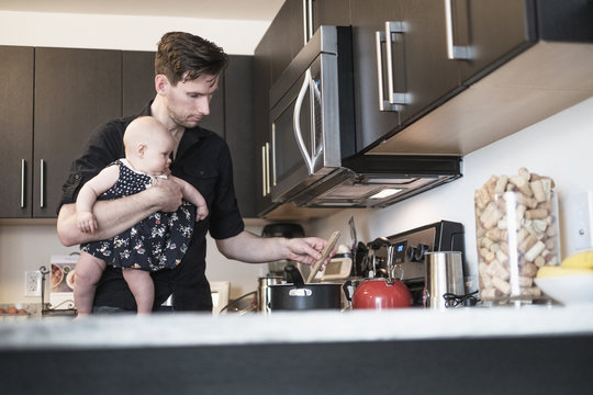 Father holding baby daughter (2-5 months) while stirring food
