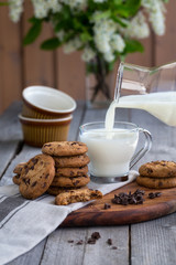 Chocolate chip cookies with milk on old rustic wooden table. Milk pouring.