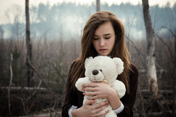 young girl hugs a teddy bear on the background of burnt forest