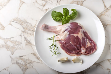 Raw uncooked duck leg on plate with garlic and herbs