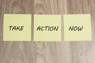 Take Action Now text on yellow sticky notes brown wooden background 