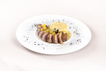 Luxurious dish with slices of duck breast, pineapple pieces, sweet sauce, with potato puree and parmesan, decorated with eatable flowers and red and green leafs, placed on white plate, light backgroun
