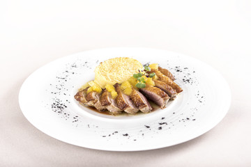 Luxurious dish with slices of duck breast, pineapple pieces, sweet sauce, with potato puree and parmesan, decorated with eatable flowers and red and green leafs, placed on white plate, light backgroun