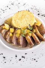 Luxurious dish with slices of duck breast, pineapple pieces, sweet sauce, with potato puree and parmesan, decorated with eatable flowers and red and green leafs, placed on white plate, light backgroun