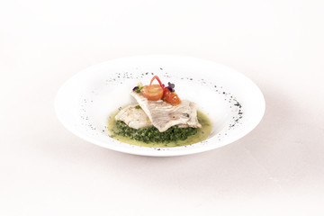 Perch fillet with spinach, sauce and tomato, decorated with eatable flowers and red leafs, placed on white plate, light background, isolated