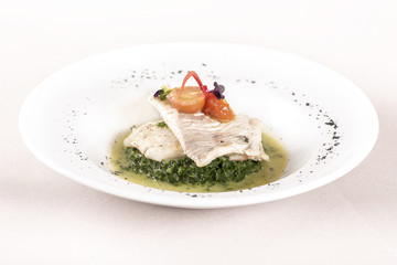 Perch fillet with spinach, sauce and tomato, decorated with eatable flowers and red leafs, placed on white plate, light background, isolated